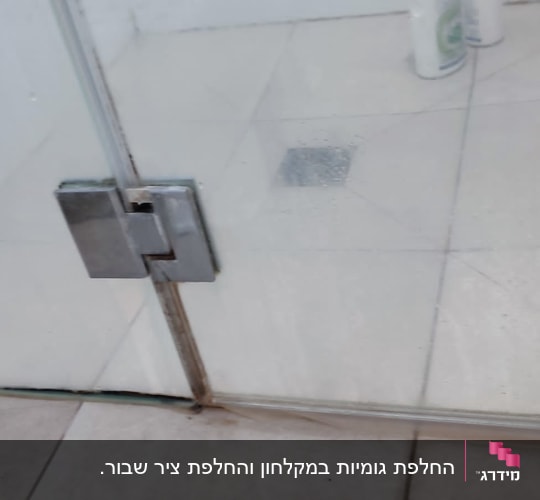 דלת זכוכית למקלחת עם בקבוקי שמפו על הרצפה